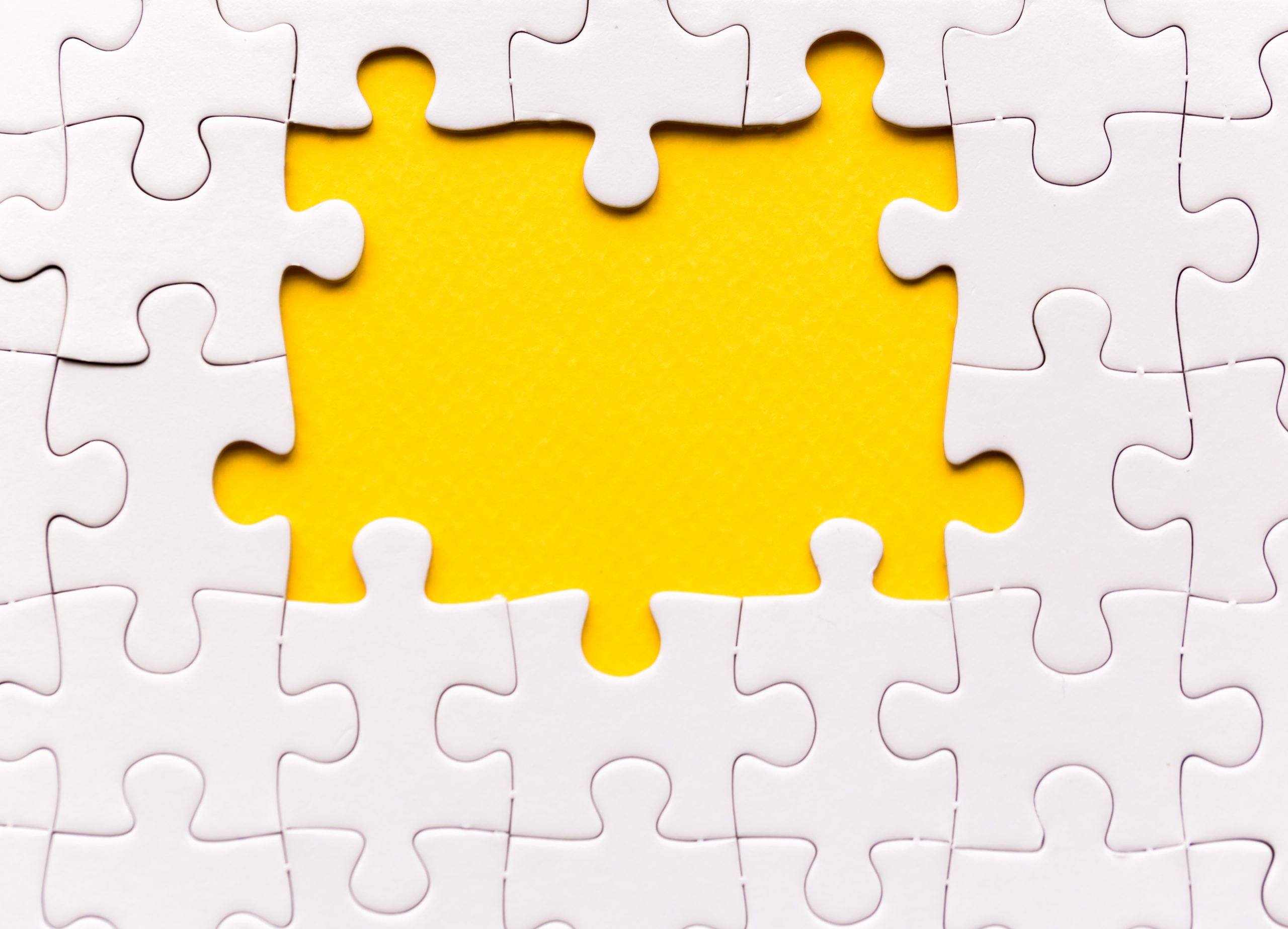 Copy space of unfinished white jigsaw puzzle pieces. One missing jigsaw piece on yellow background