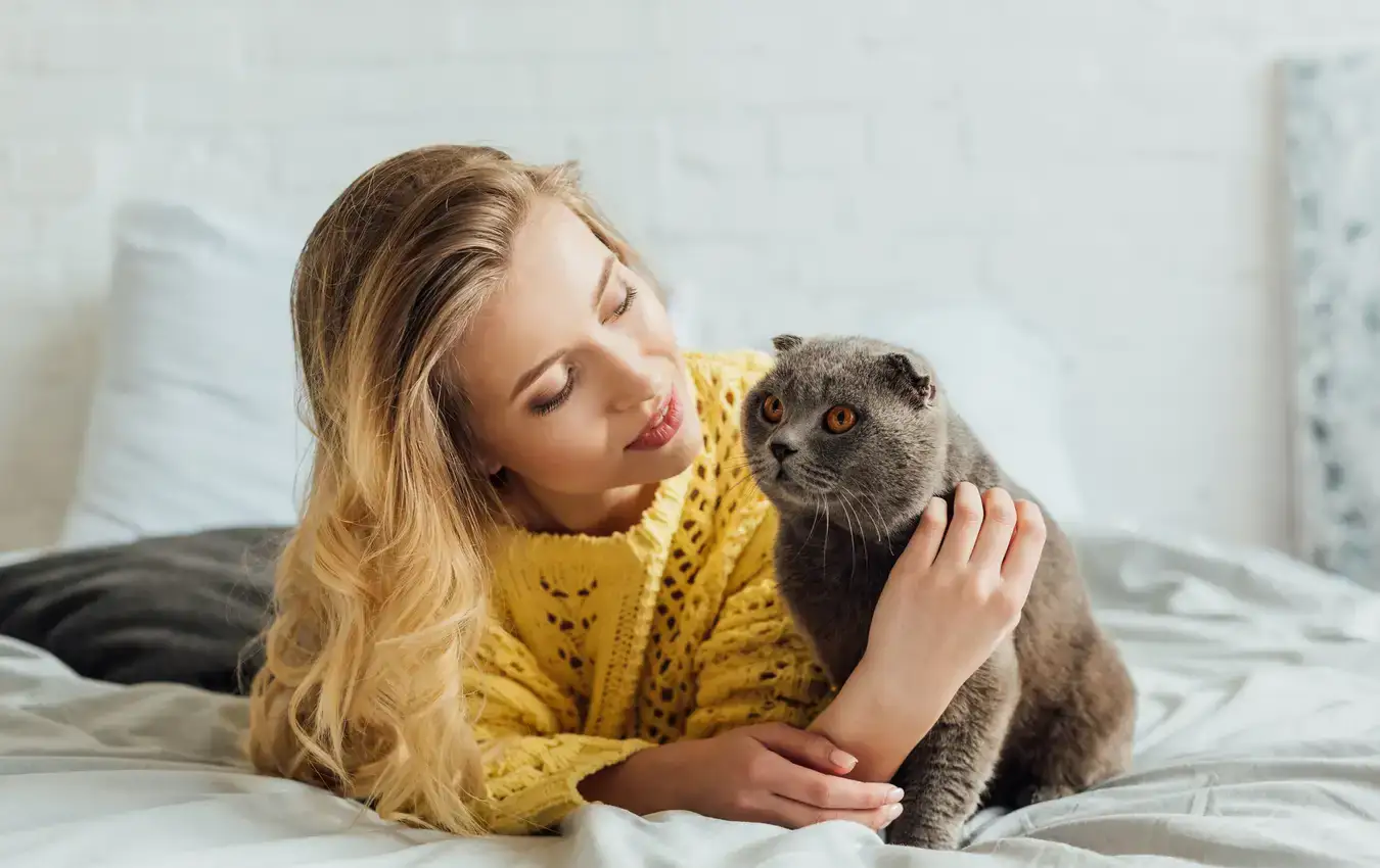 Donna che abbraccia gatto su letto con tessuti morbidi